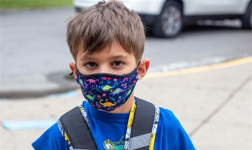 A boy wearing a blue shirt and a mask smiles